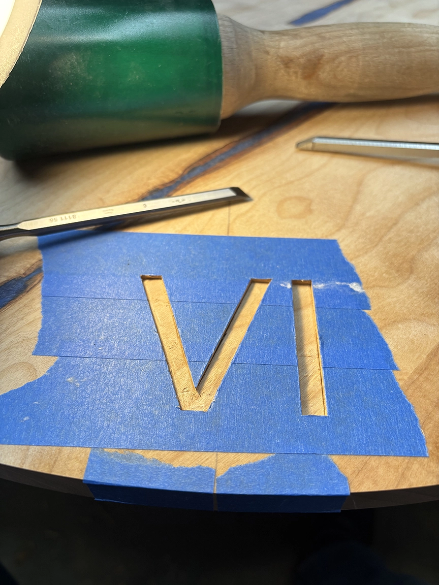 Close-up of hand-carved Roman numerals in progress on a figured wood clock face